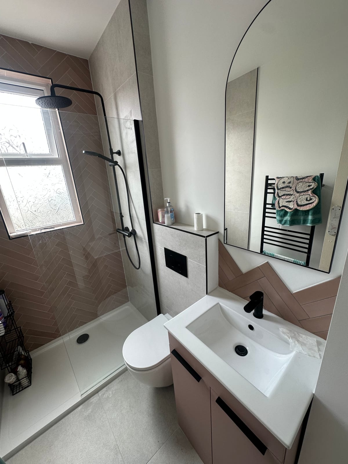 Blush pink bathroom with herringbone tiles and arched mirror
